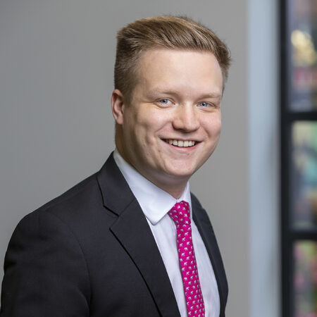 Man wearing pink tie and black suit jacket smiling at camera.